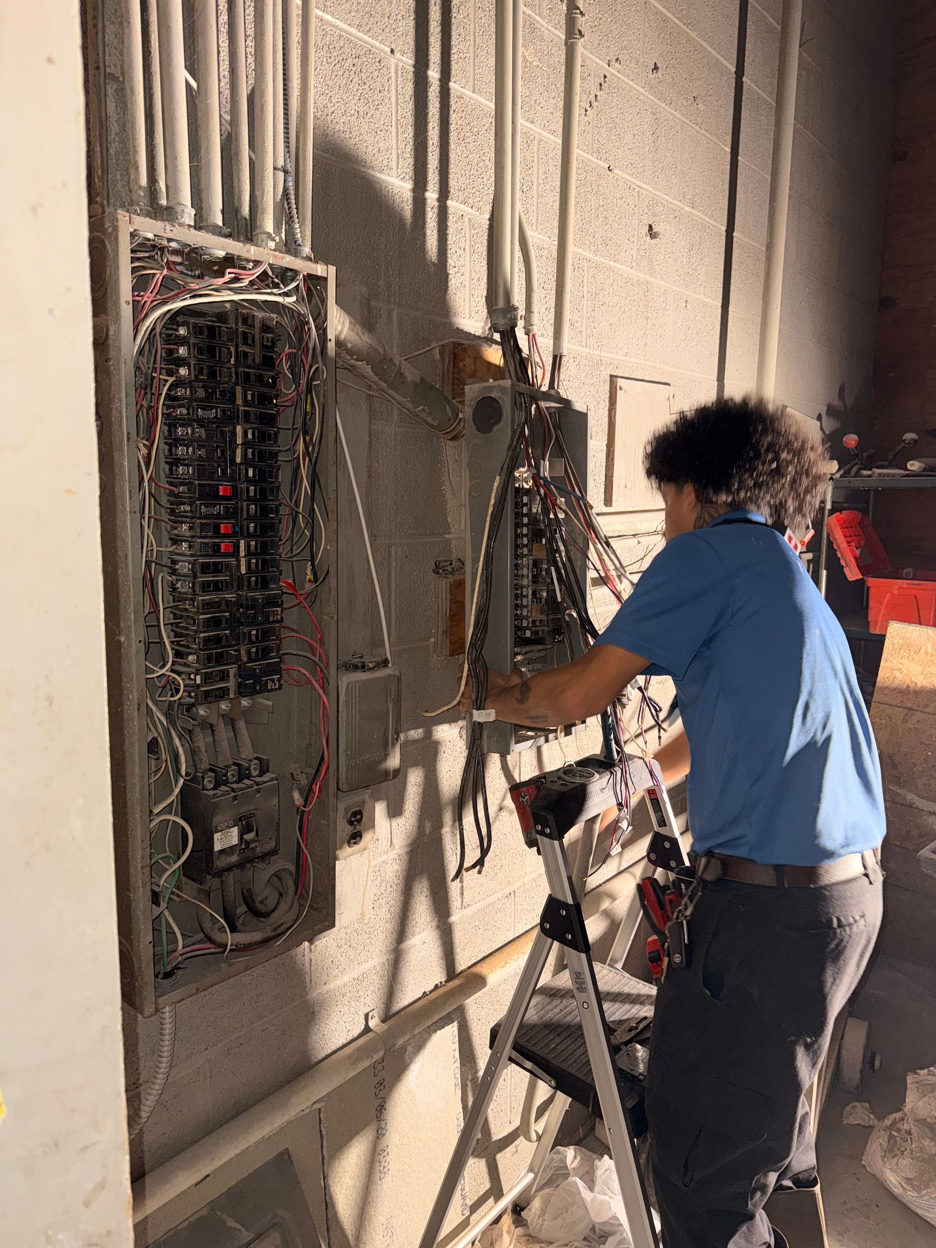 Electrician working on electrical panels mounted on a concrete wall indoors.