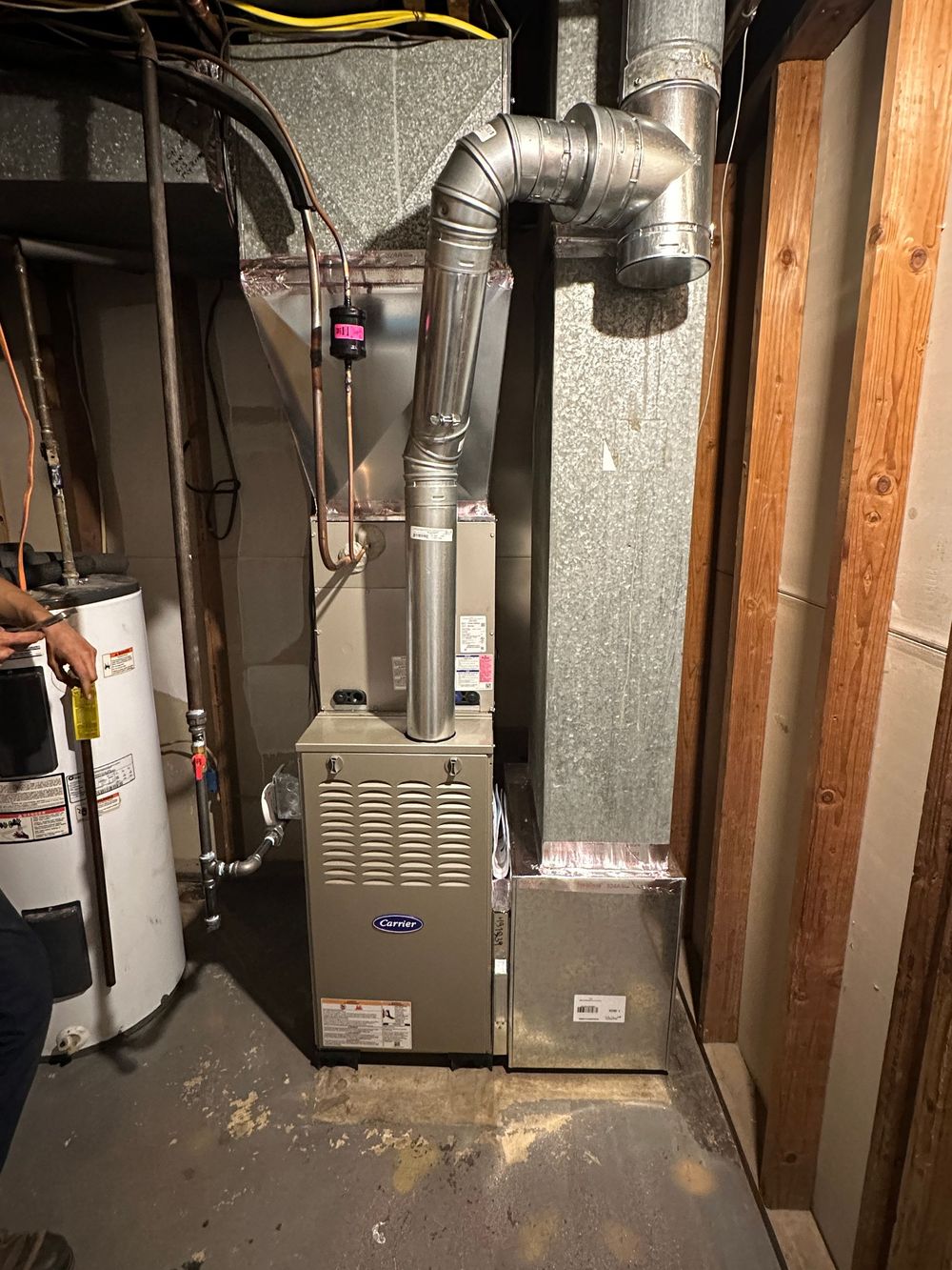 Furnace and water heater in a basement. Metal ducts and pipes are visible along with wooden framing.