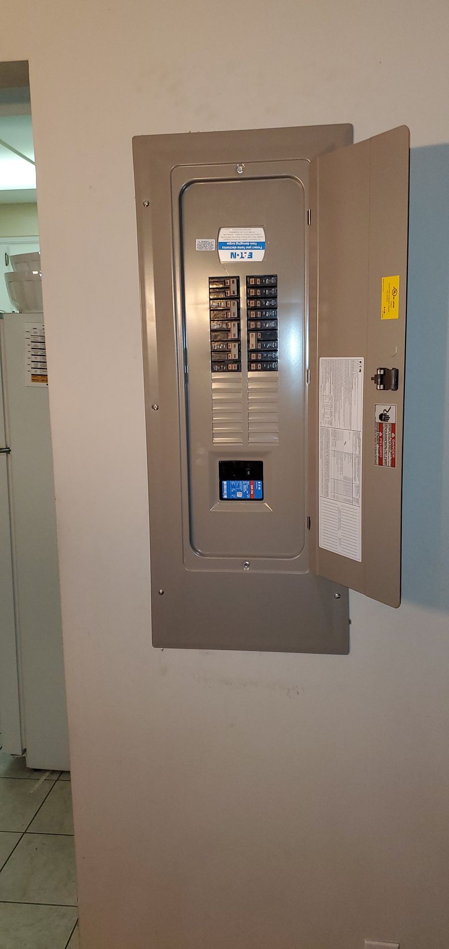 Electrical panel mounted on a light beige wall. The door is open, showing the circuit breakers.