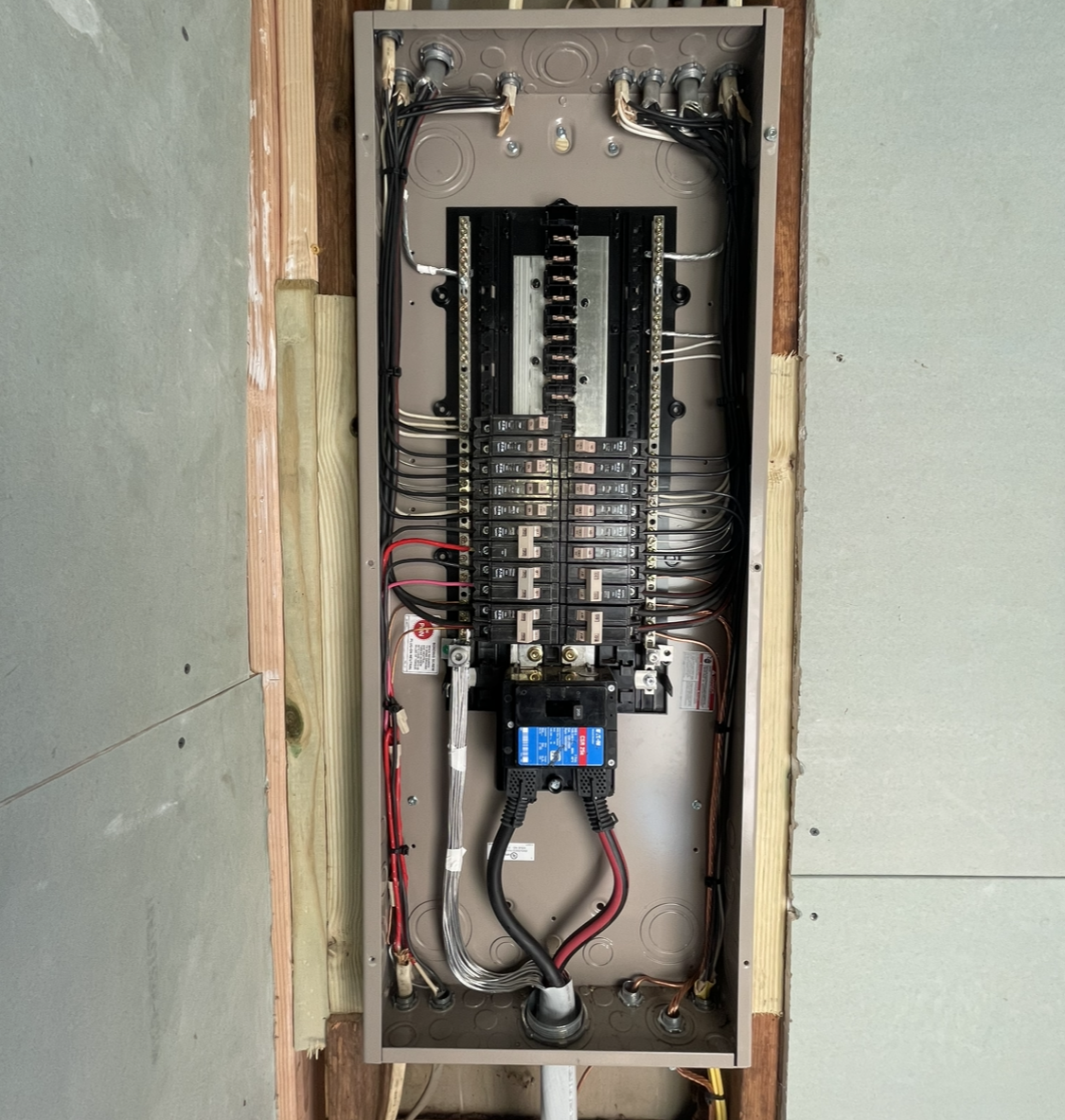 Electrical panel installed in a wall with wires and breakers.