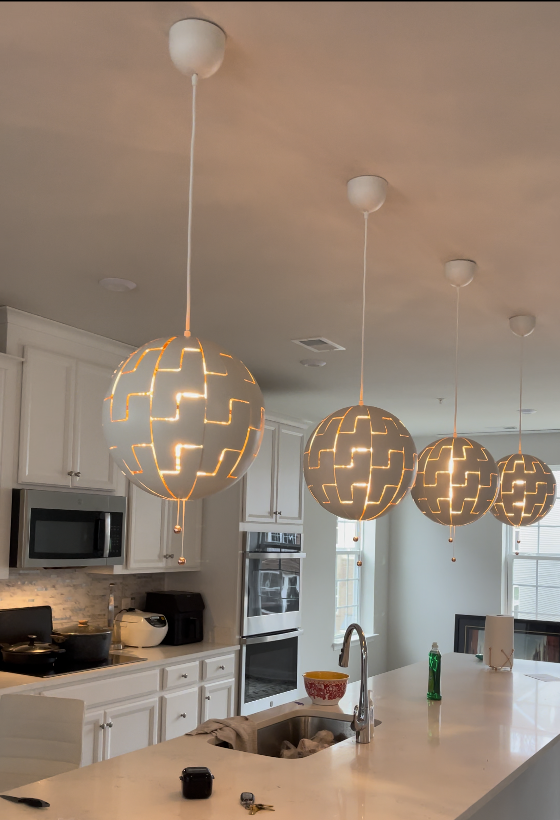 Four white globe pendant lights hanging over a kitchen island. The kitchen has white cabinets and a microwave.