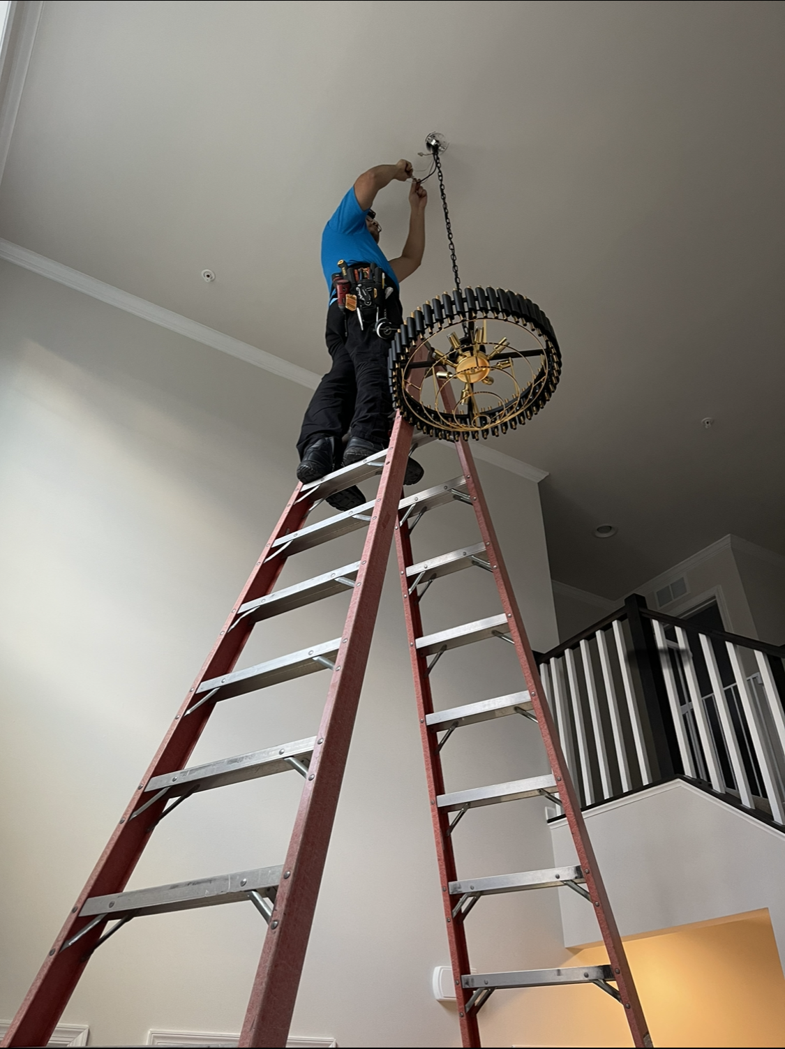Person on ladder installing chandelier in home.