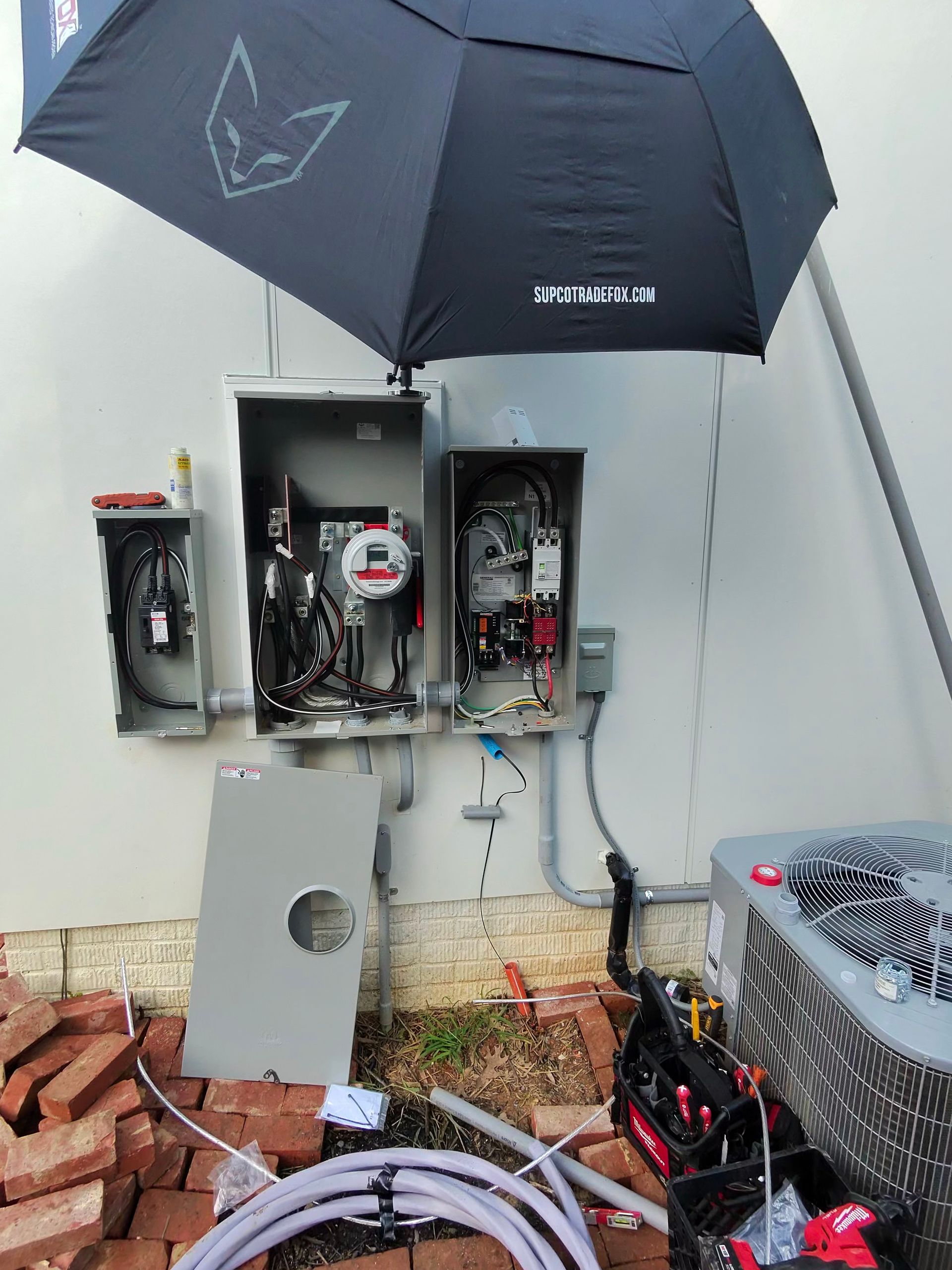Electrical panel being worked on outside, with an umbrella providing shade. Wires, tools and conduit visible.