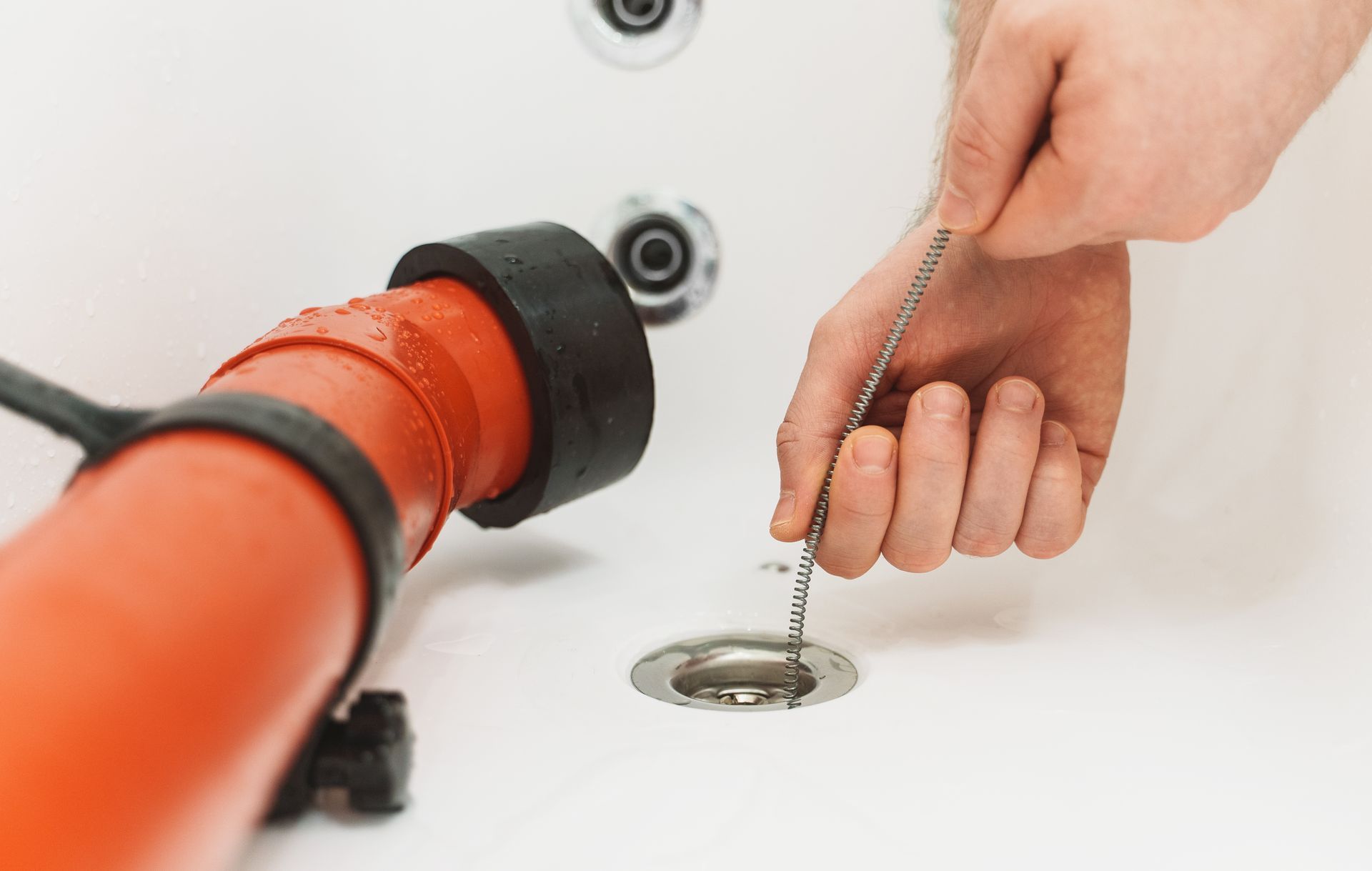 Plumber using a flexible metal snake for bathtub drain cleaning to remove hair clogs. Plumber using a flexible metal snake for bathtub drain cleaning to remove hair clogs.