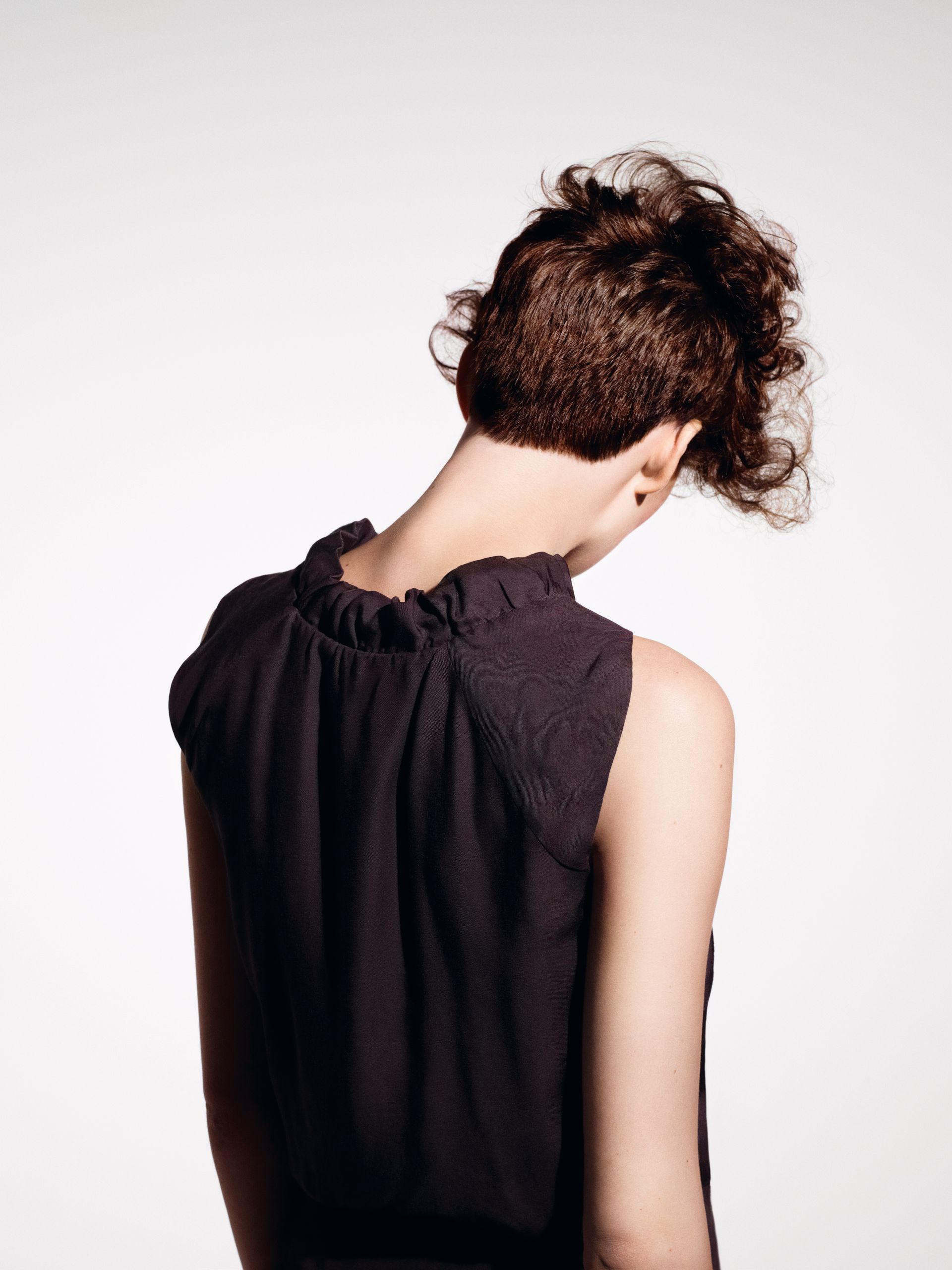 Woman with a shaved head and a large, pink-dyed, up-do. She's wearing dark makeup and gazing pensively to the side.