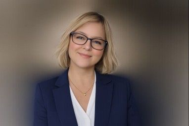 Portrait of a smiling woman in glasses and a navy blazer against a blurred background
