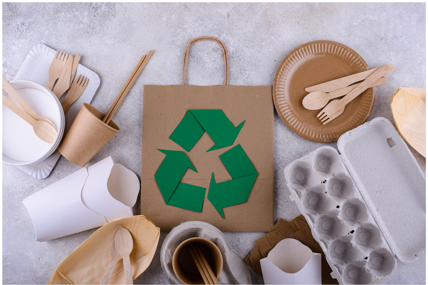 A brown paper bag with a green recycling symbol on it is surrounded by wooden utensils and plates.