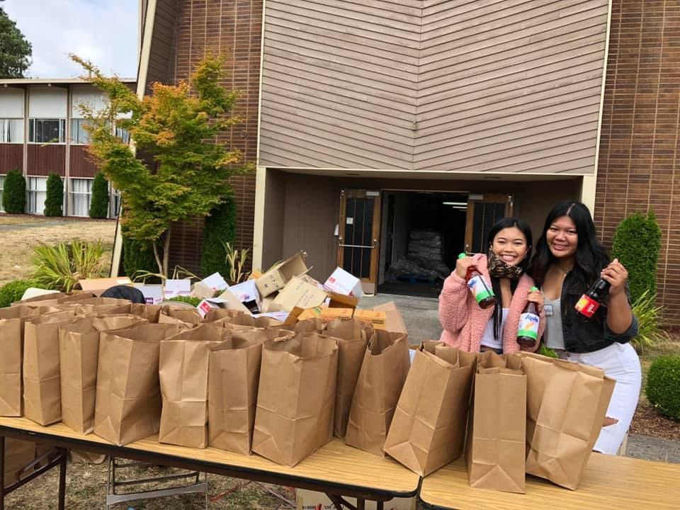 Two women are standing next to a table filled with paper bags.