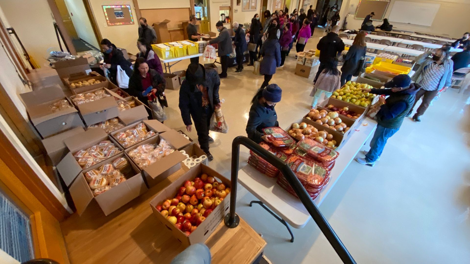 A group of people are standing in a room filled with boxes of food.