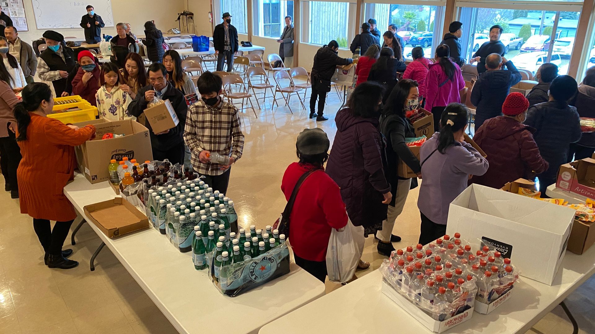 A large group of people are standing around tables filled with bottles of water.