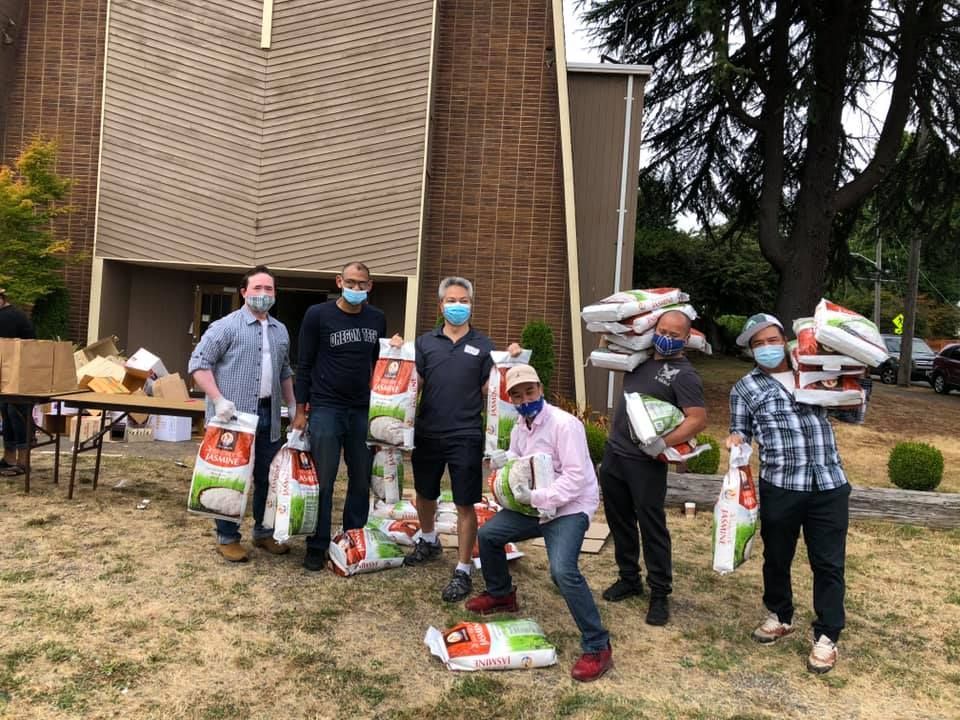 A group of men wearing face masks are standing in front of a building holding bags of food.