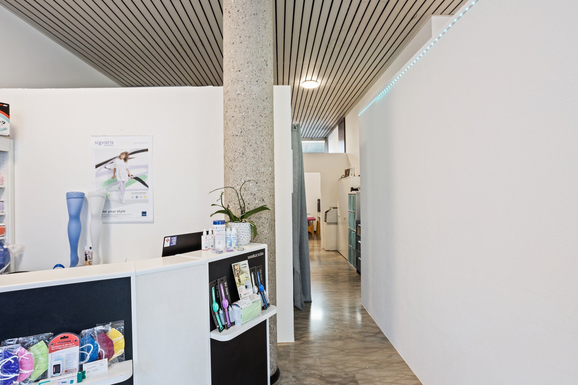 Area reception con pareti bianche, colonna e un corridoio che conduce a un ufficio.