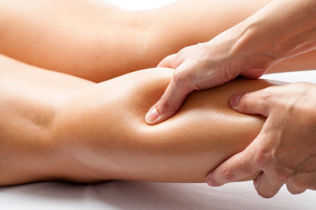 Hands massaging a person's calf muscle. Close-up view. Light skin tone. White background.