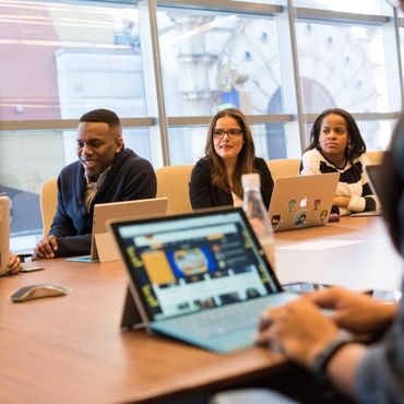 A group of people are sitting around a table with laptops