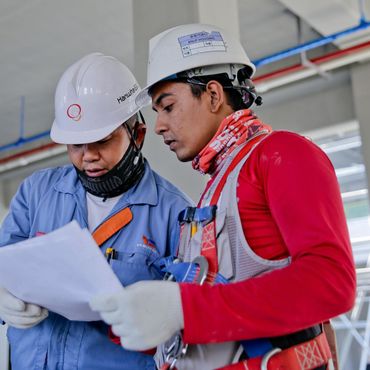 Two men wearing hard hats are looking at a piece of paper