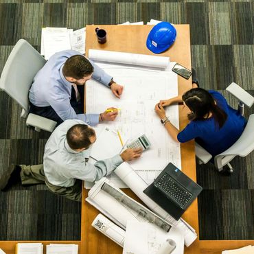 A group of people are sitting around a table looking at blueprints