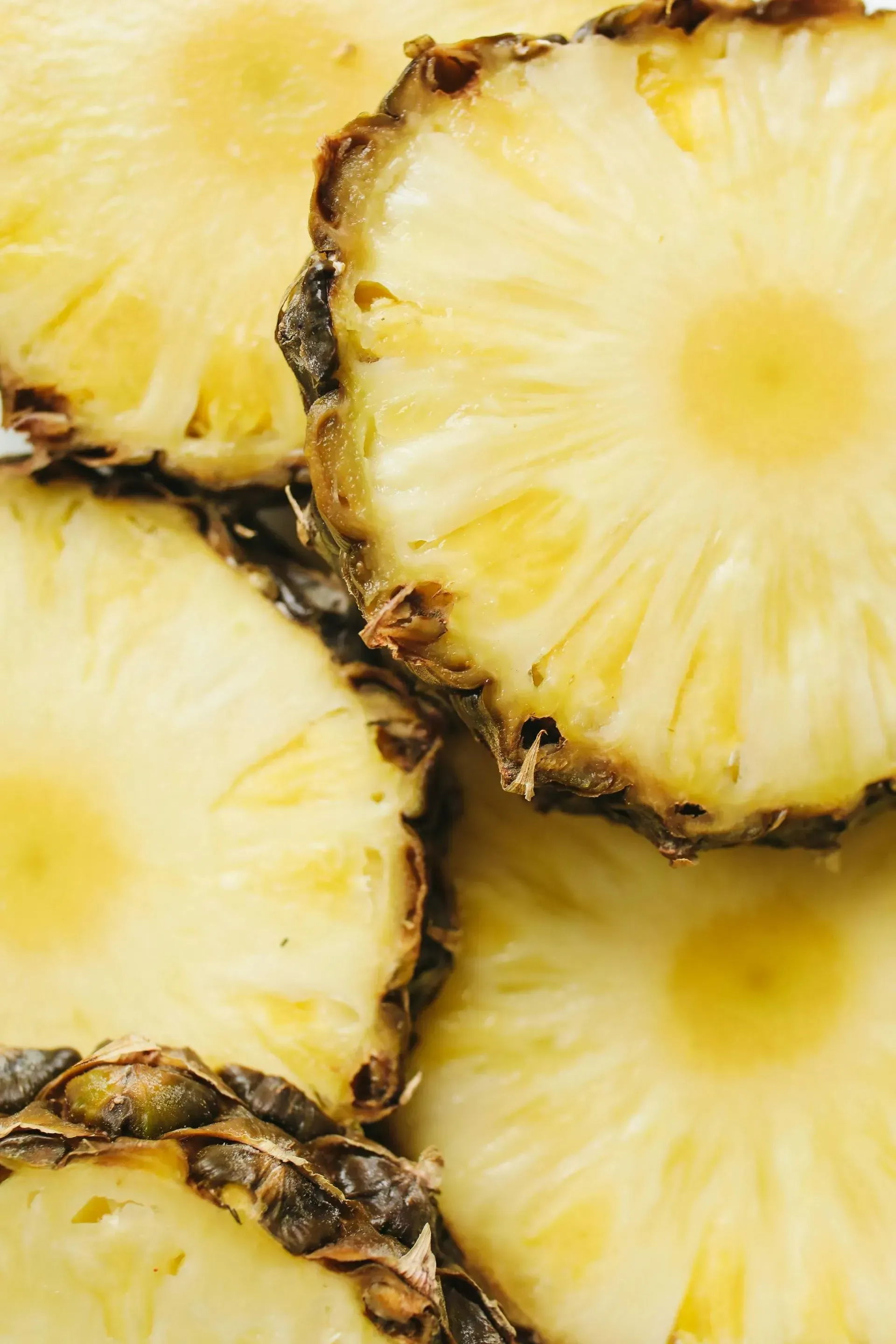 Close-up of sliced pineapple rings with yellow flesh and dark brown edges.