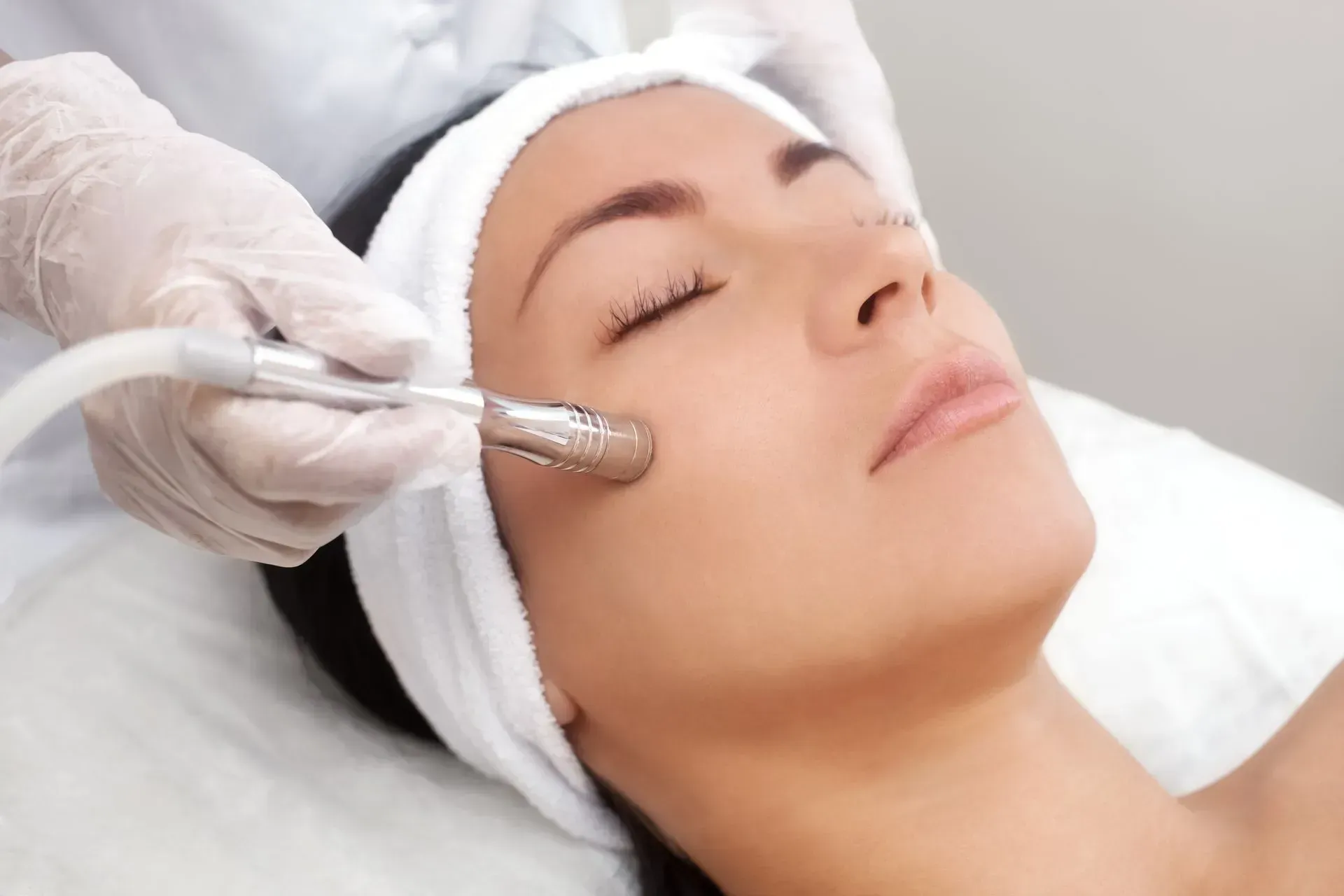 Facial treatment with gloved hand using a metal skincare tool on a relaxed client lying down