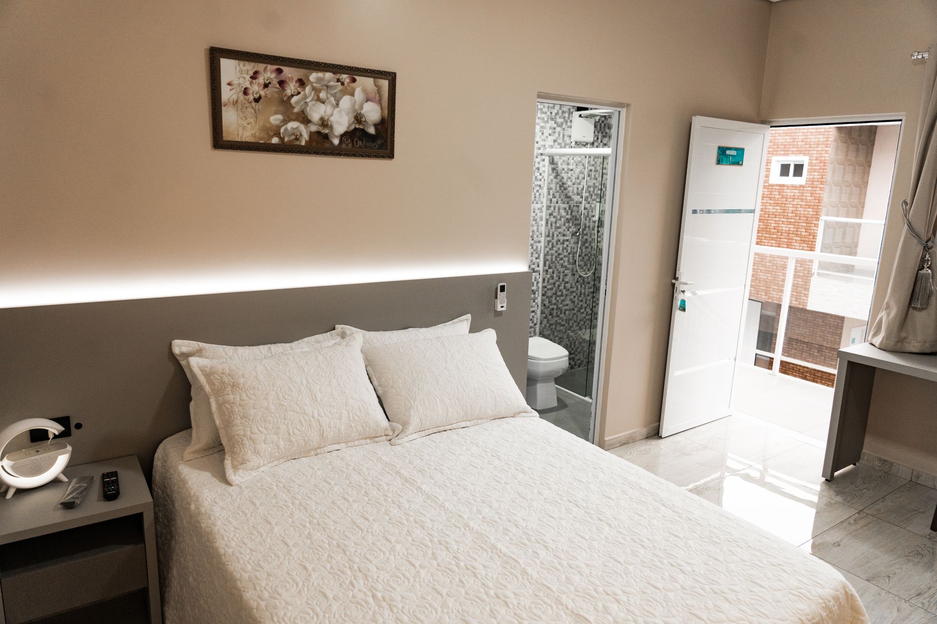 Um quarto com uma cama, mesa de cabeceira, banheiro e um quadro na parede. MD Recanto Hotel