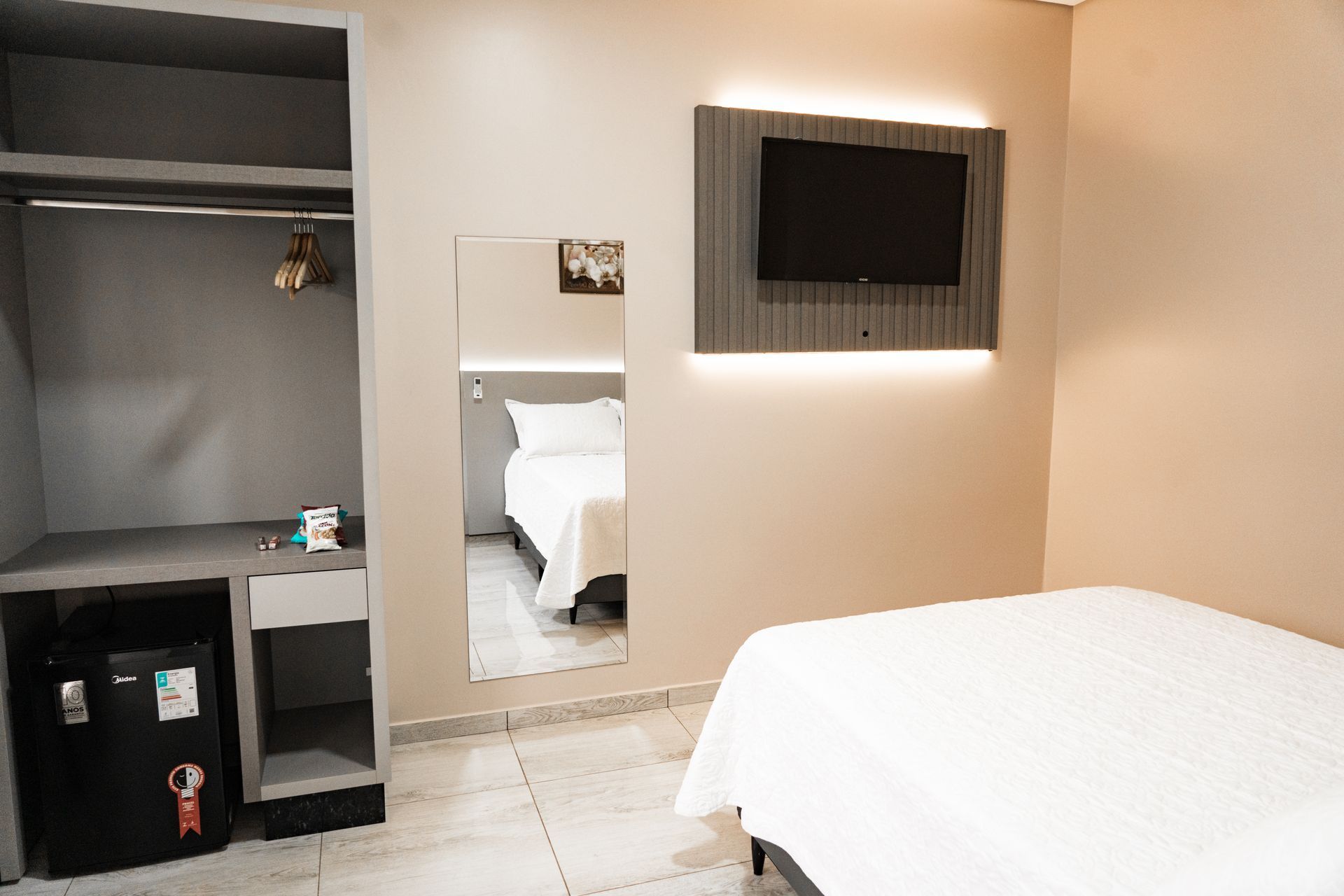 Um quarto de hotel com cama, televisão, geladeira e espelho. MD Recanto Hotel