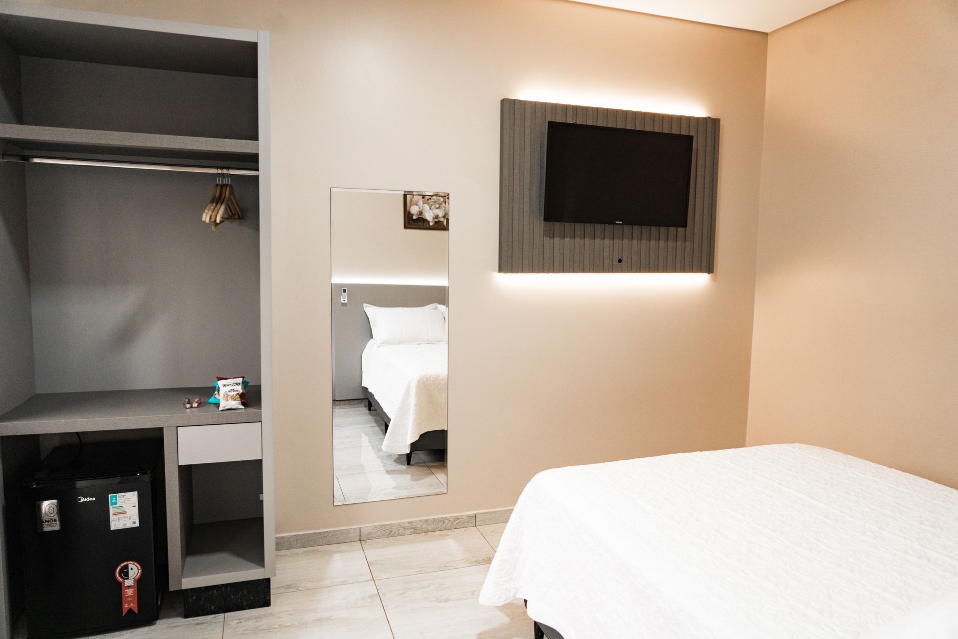 Um quarto de hotel com cama, televisão, geladeira e espelho.MD Recanto Hotel