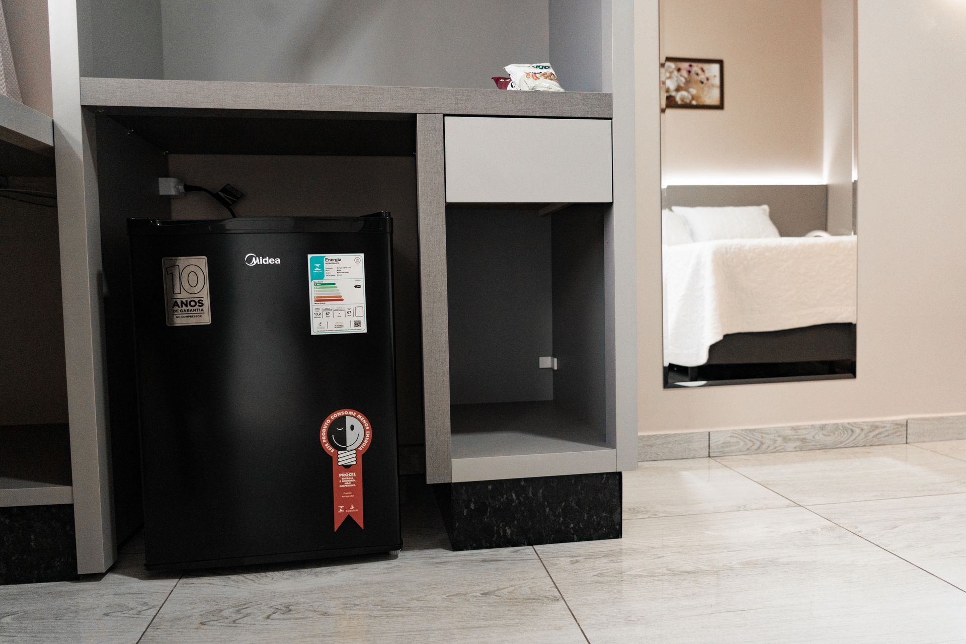 Uma pequena geladeira preta está ao lado de uma mesa em um quarto de hotel. MD Recanto Hotel
