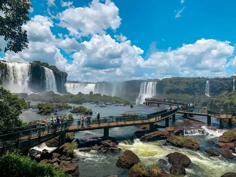 Uma ponte sobre um rio com uma cachoeira ao fundo. MD Recanto Hotel