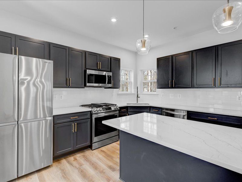 A kitchen with black cabinets , stainless steel appliances , and a large island.