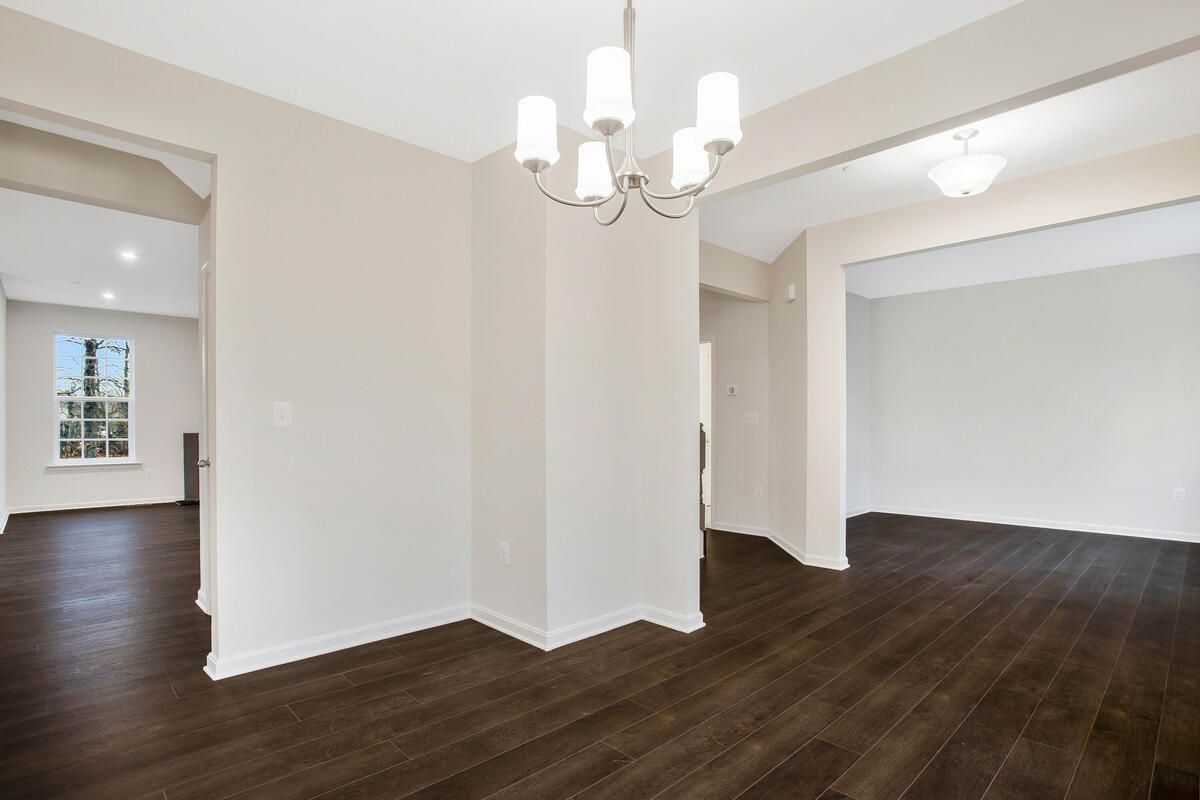 An empty dining room with hardwood floors and a chandelier.