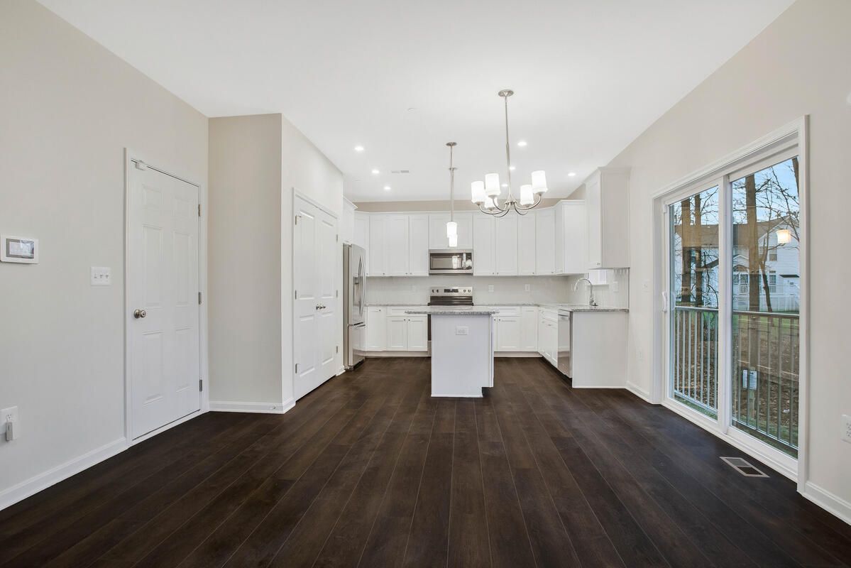 An empty living room with a kitchen in the background.