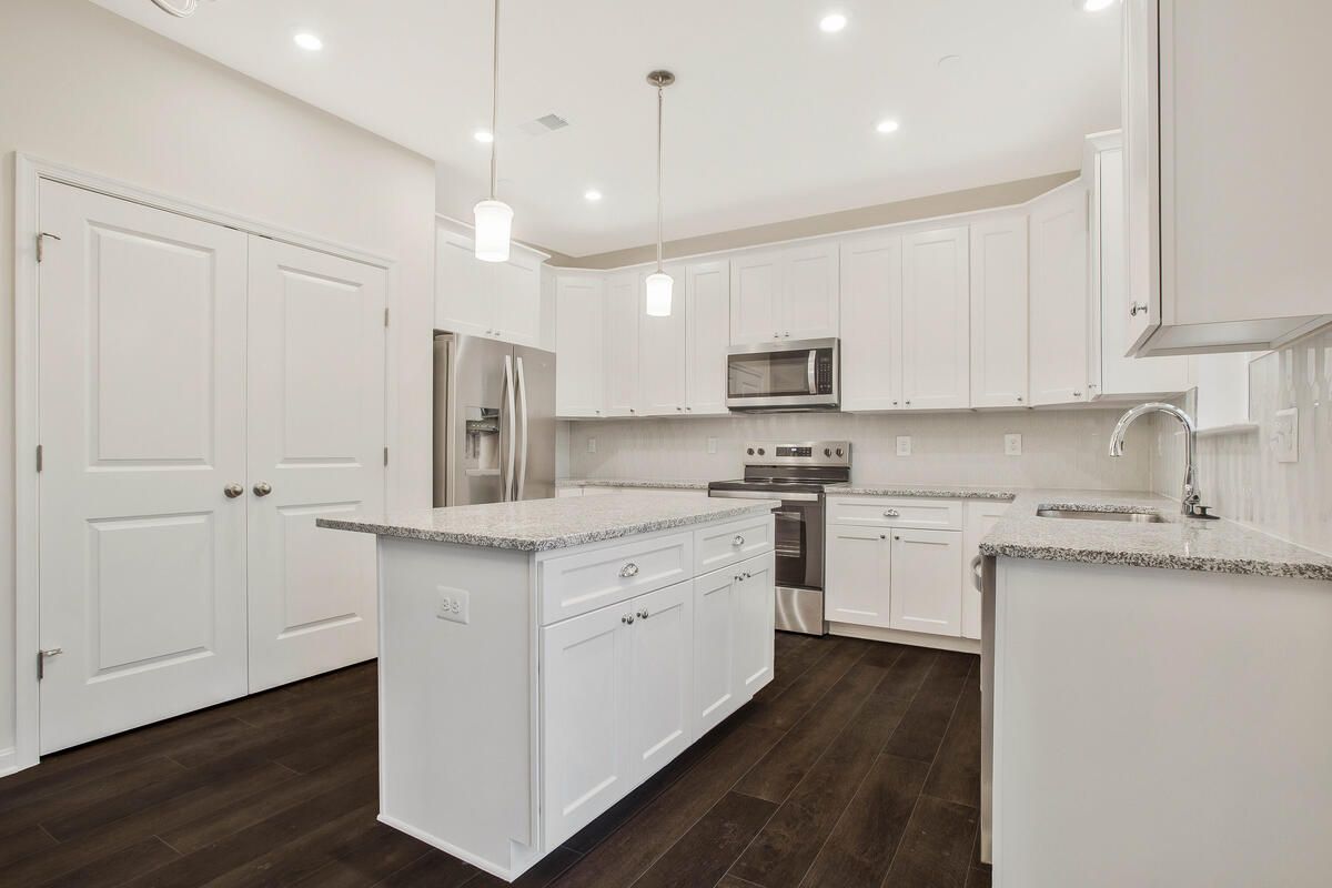 A kitchen with white cabinets , granite counter tops , stainless steel appliances and a large island.