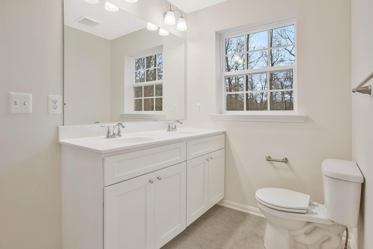 A bathroom with a toilet , sink , mirror and window.