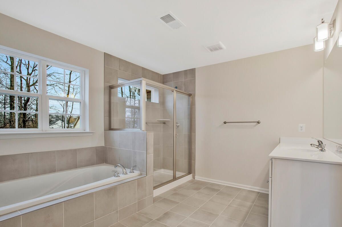 A bathroom with a tub , sink , shower and window.