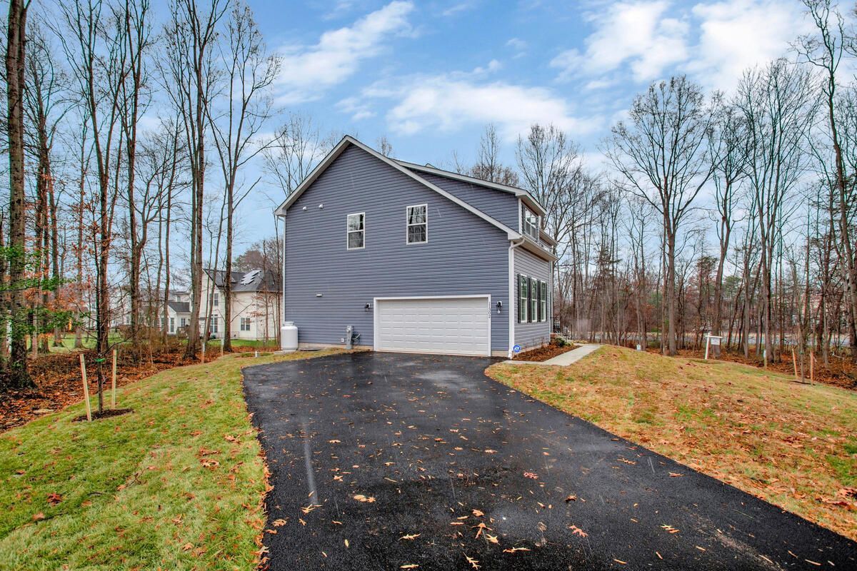 A house with a garage and a driveway in front of it surrounded by trees.
