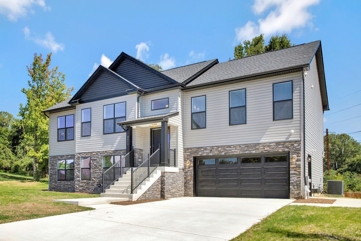 A large white house with a black garage door is sitting on top of a lush green hillside.