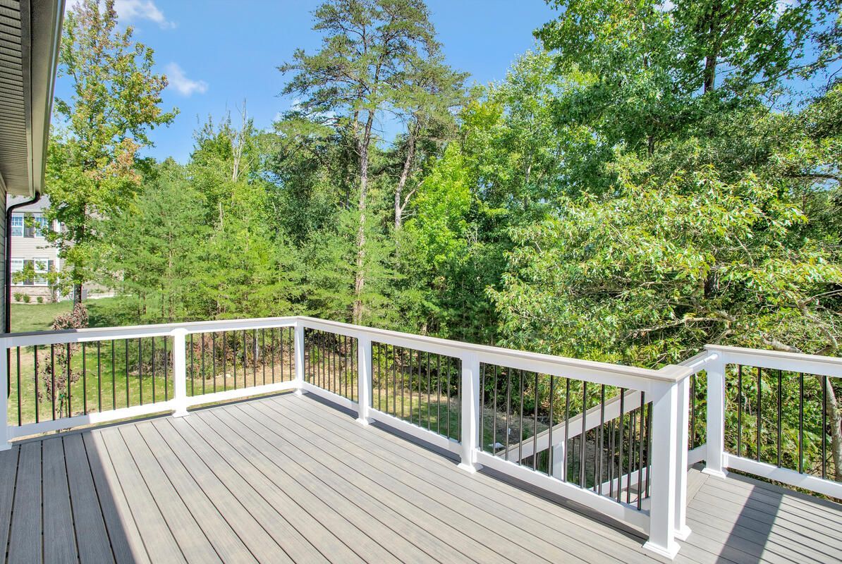 An empty deck with a white railing and trees in the background.