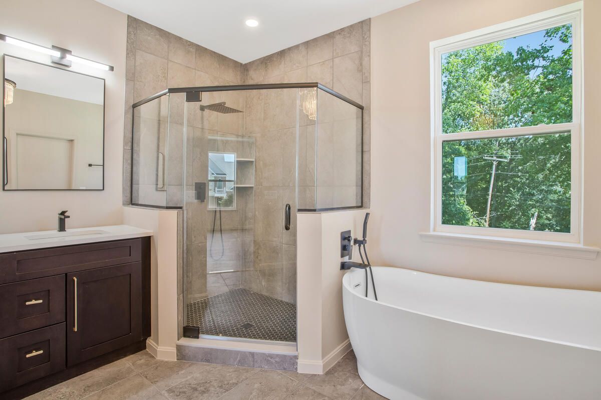 A bathroom with a tub , sink , shower and window.