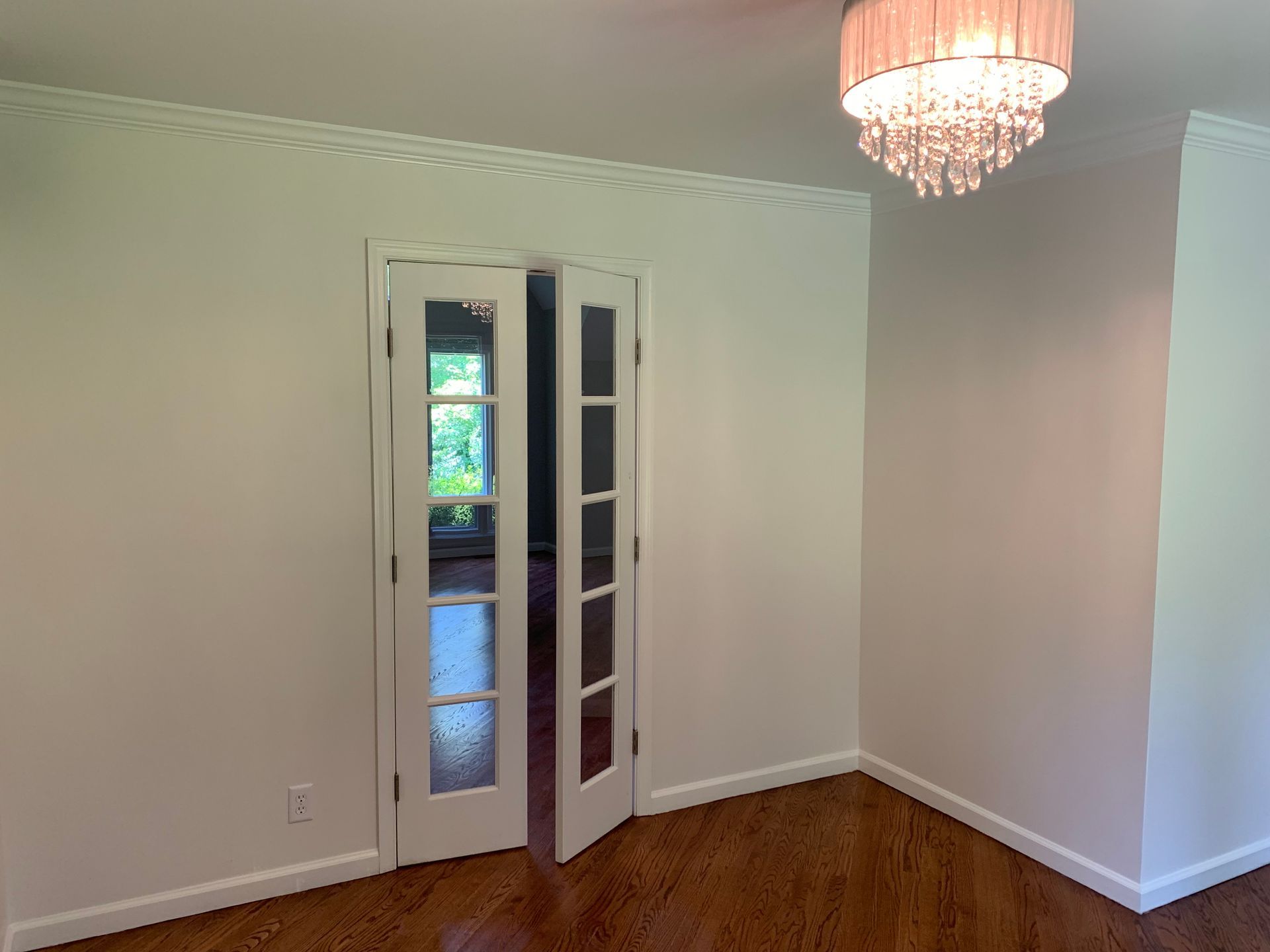 An open, double-door entry way with glass panes, in a room with a wood floor, crown molding, and a chandelier.