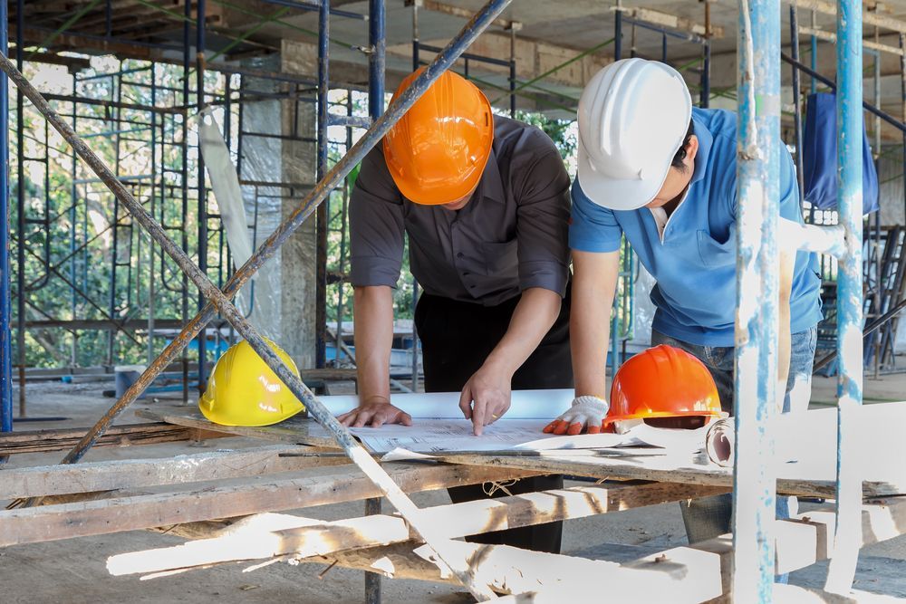 two construction workers are looking at a blueprint at a construction site .