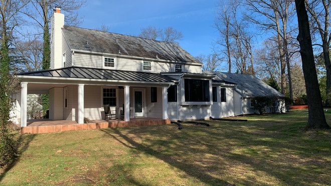 the back of a white house with a porch and trees in the background .