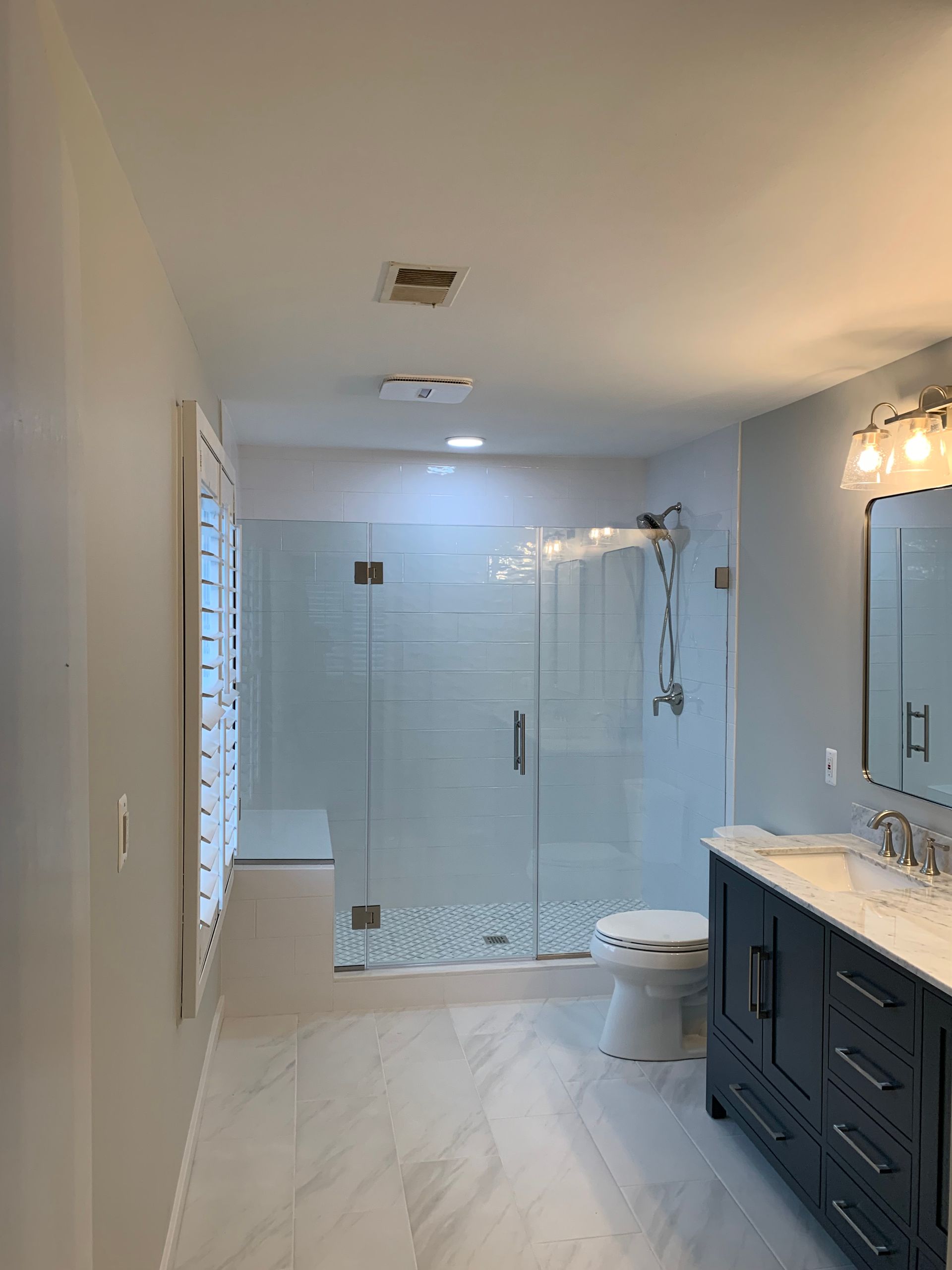 A newly renovated bathroom with a large glass shower, dark blue vanity, and white tile floor.