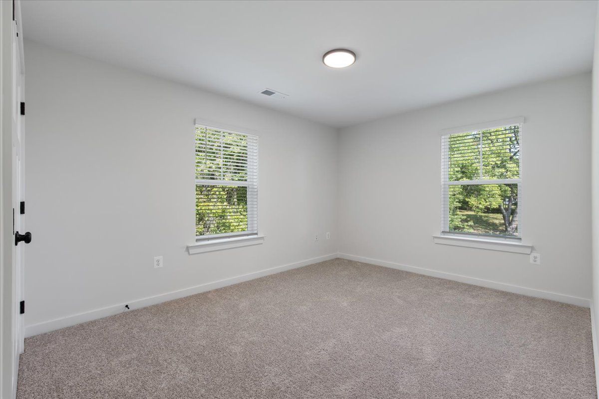 An empty bedroom with two windows and a carpeted floor.