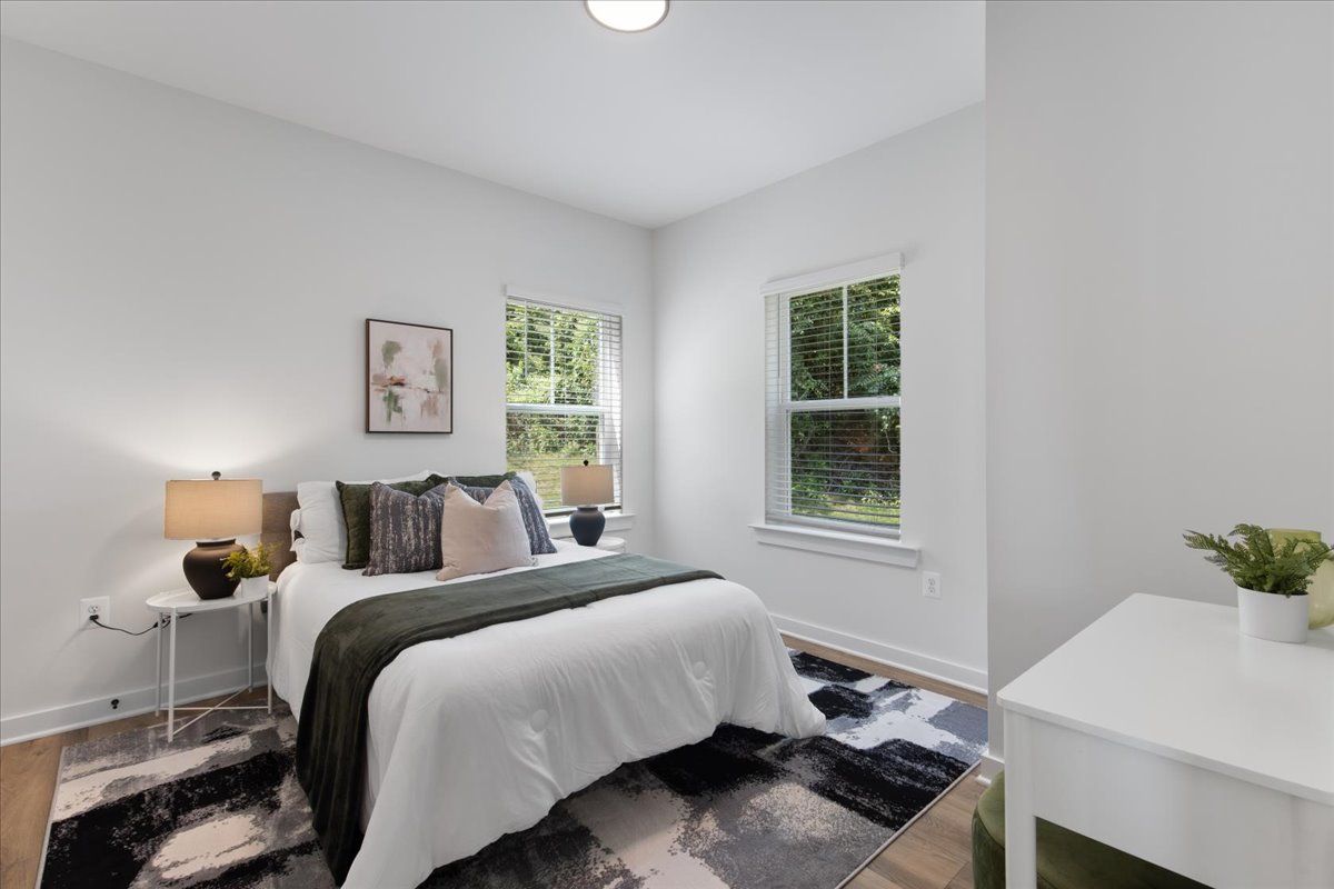 A bedroom with a bed , nightstand , rug and window.