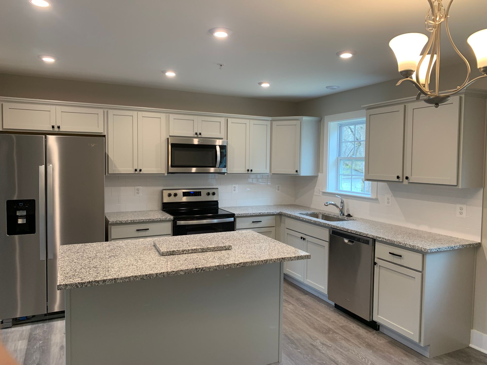 Modern kitchen with light gray cabinets, stainless steel appliances, and granite countertops. An island sits in the center.