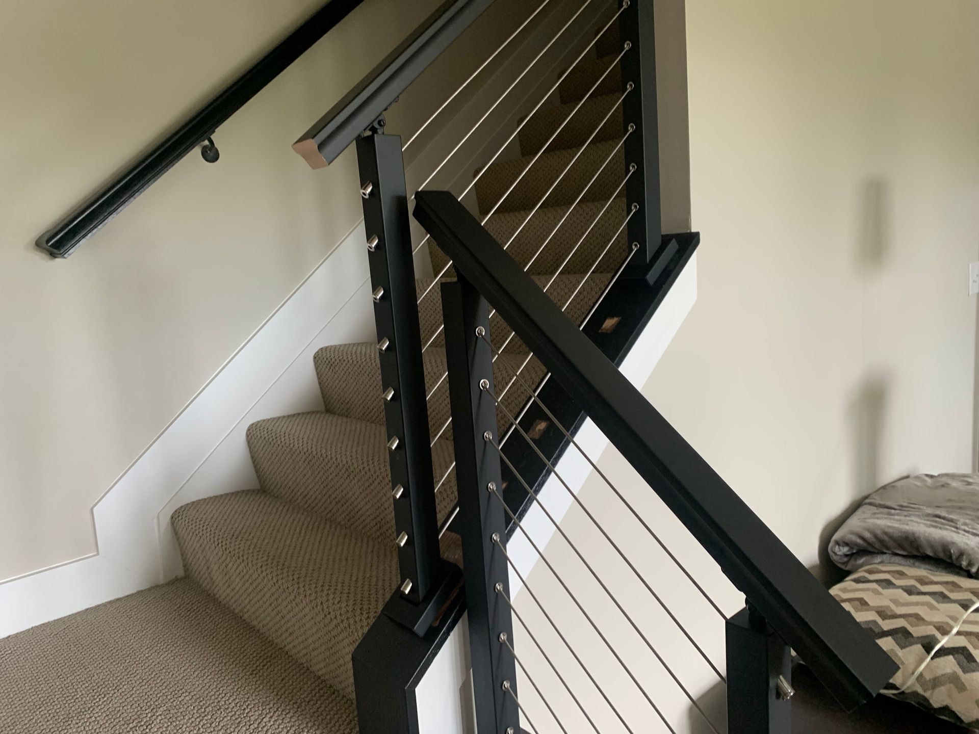 Staircase with black railing and cable wires; beige carpeted steps. Handrail on left. Modern interior.