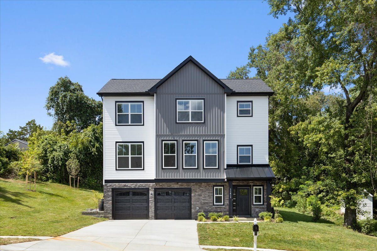 A large white and gray house with three garages is sitting on top of a lush green hill.