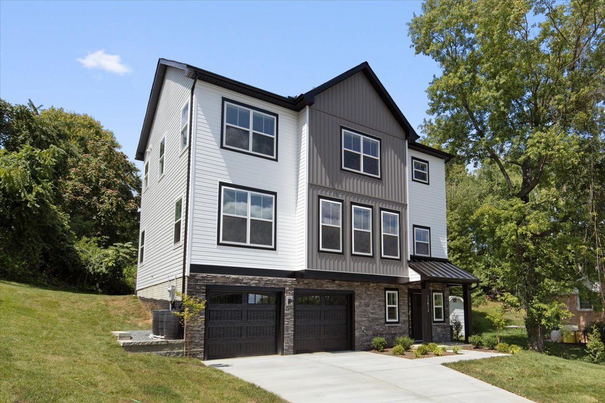 A large white and brown house with two garages is sitting on top of a grassy hill.