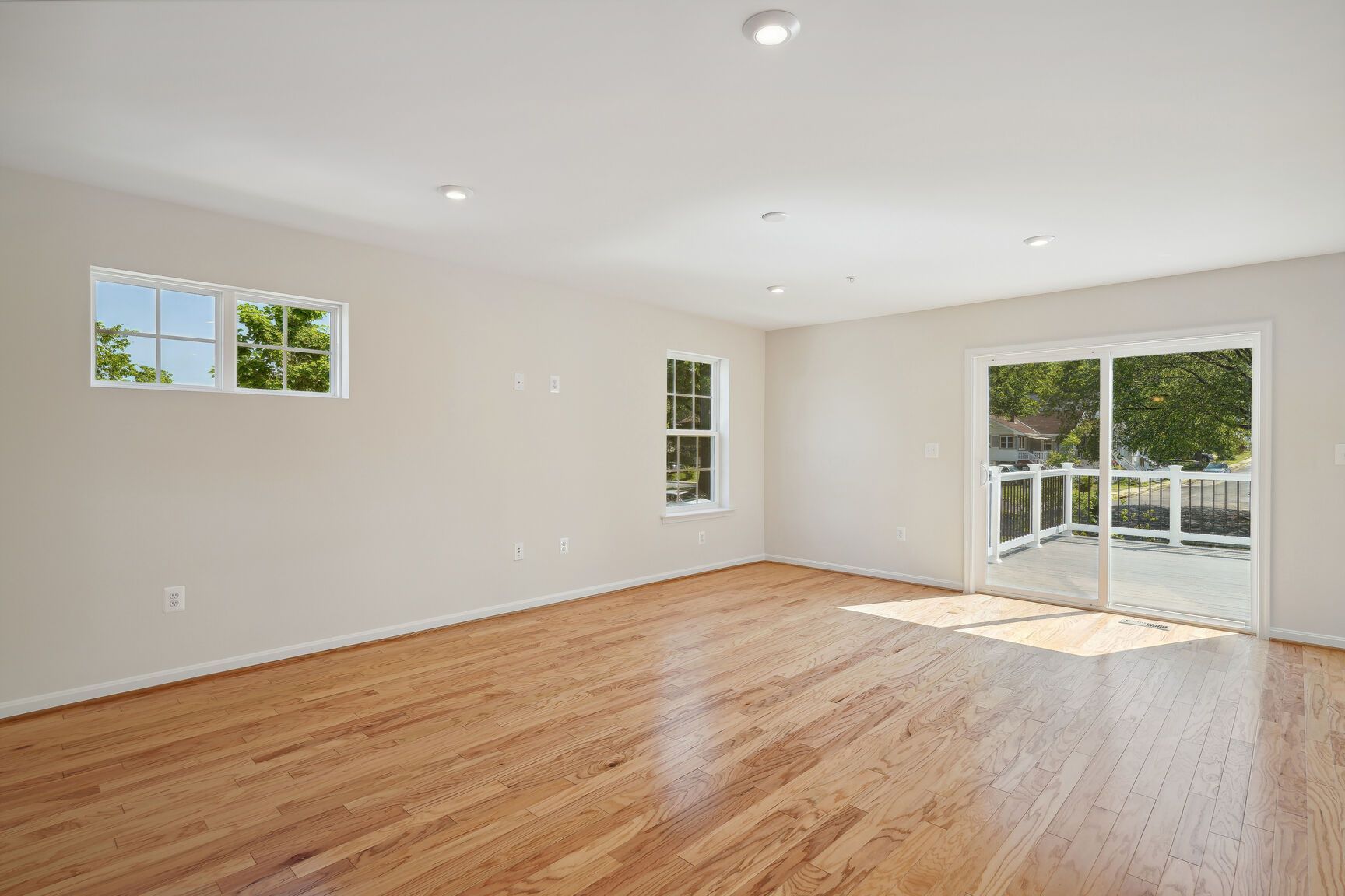 An empty living room with hardwood floors and sliding glass doors.