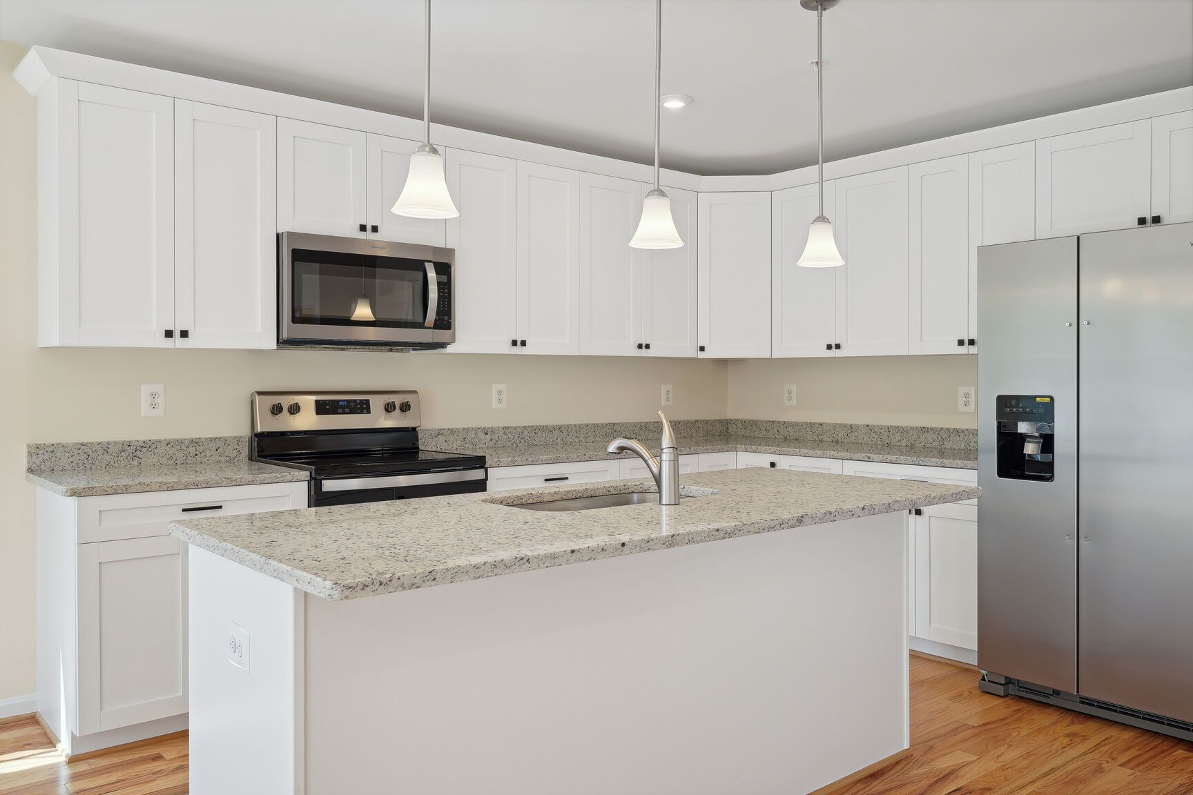 A kitchen with white cabinets , granite counter tops , stainless steel appliances and a large island.