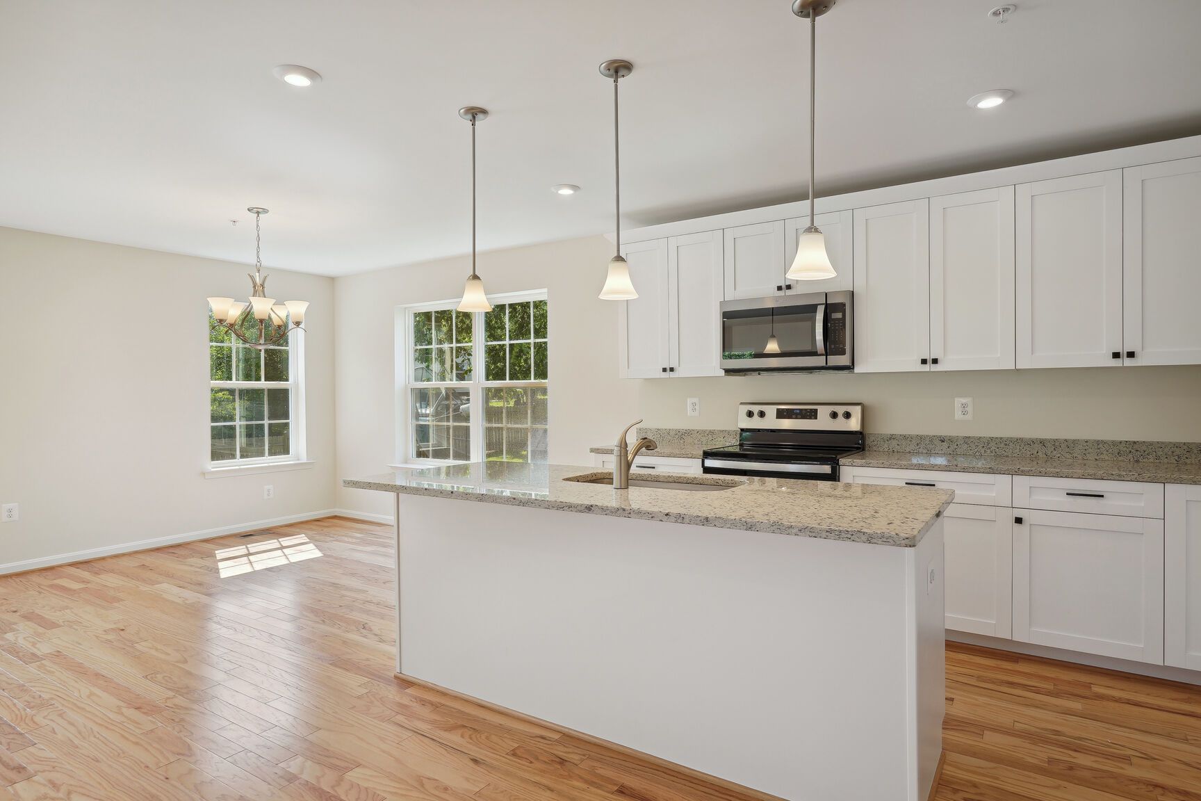 An empty kitchen with white cabinets , granite counter tops , stainless steel appliances , and hardwood floors.